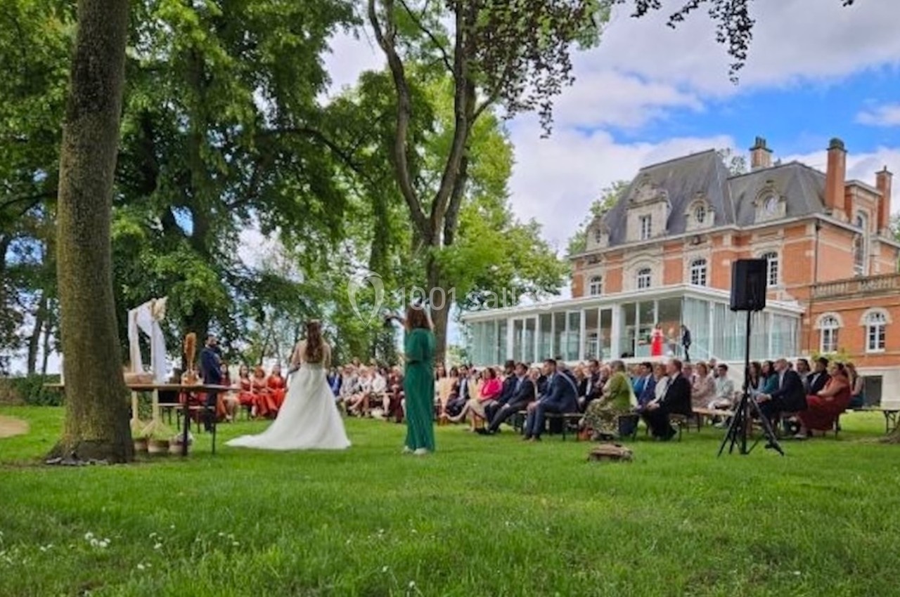 Cérémonie en plein air dans un parc, avec des invités assis face à une mariée et un officiant, devant un manoir.