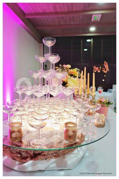 Tour de coupes en verre empilées pour un service de champagne, entourée de bougies et décorations florales.