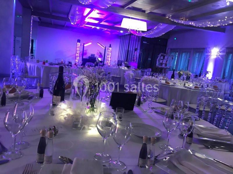 Salle de réception décorée avec des tables dressées, éclairage violet et ambiance festive.