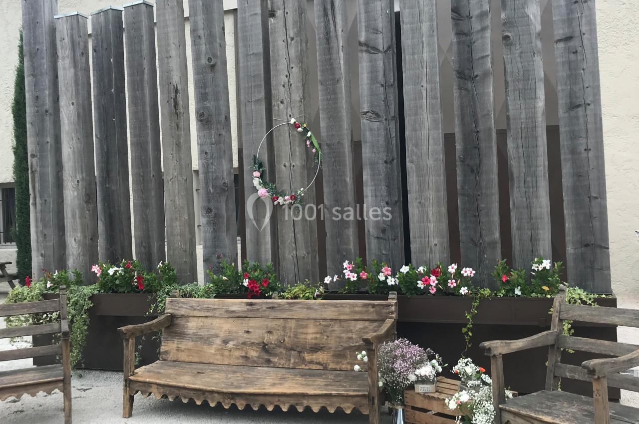Bancs en bois devant une clôture en planches verticales, décorée de fleurs et d'une couronne florale suspendue.