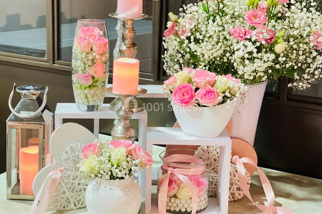 Arrangement floral avec roses roses, gypsophiles et bougies, présenté sur des supports décoratifs dans un cadre intérieur.