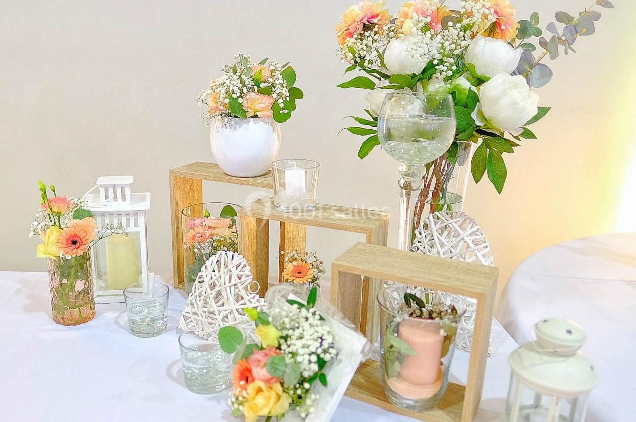 Décoration de table avec fleurs colorées, bougies et cadres en bois sur une nappe blanche.