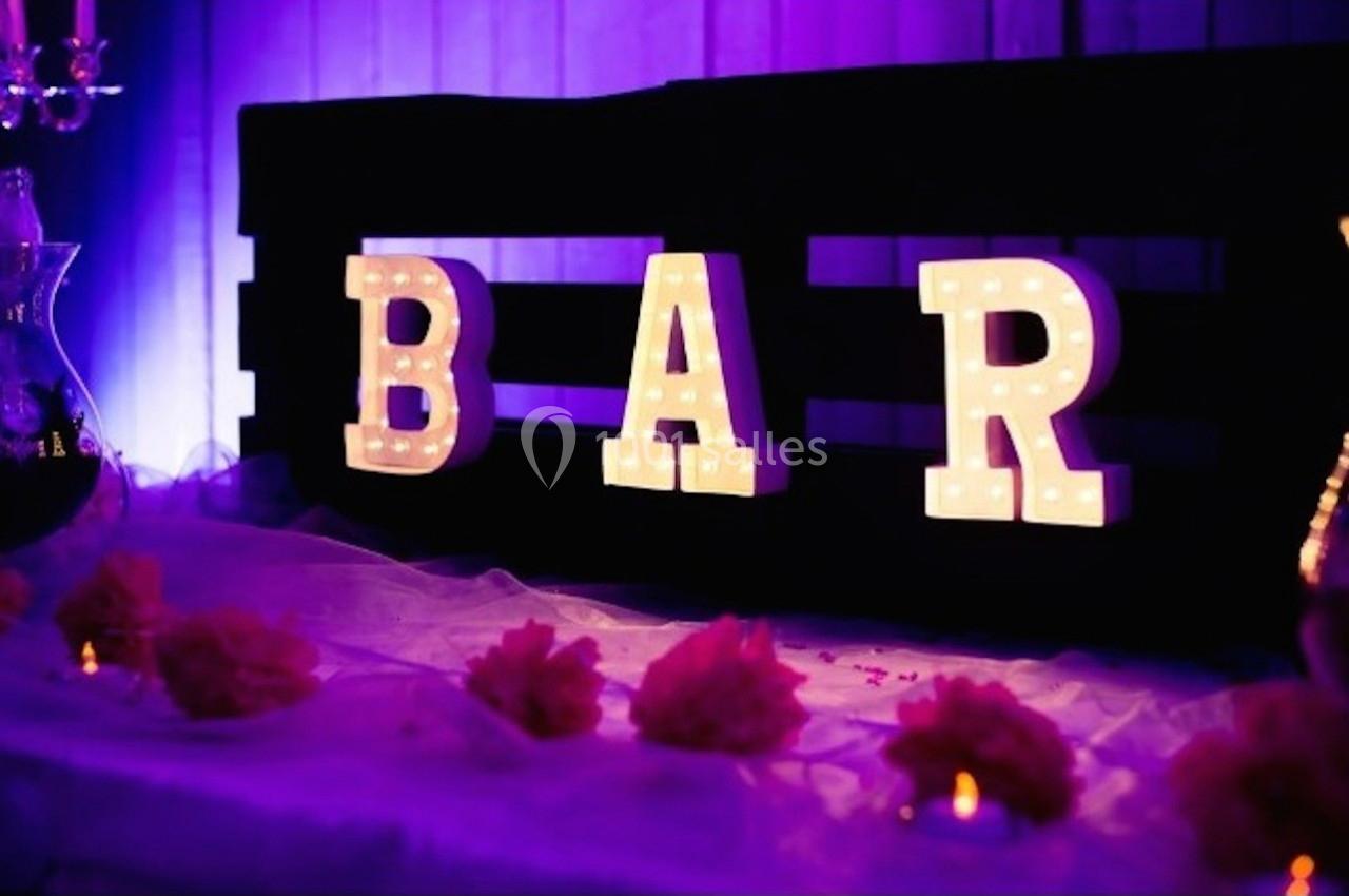 Lettres lumineuses formant le mot ’BAR’ sur une table décorée de fleurs et éclairée par une lumière violette.