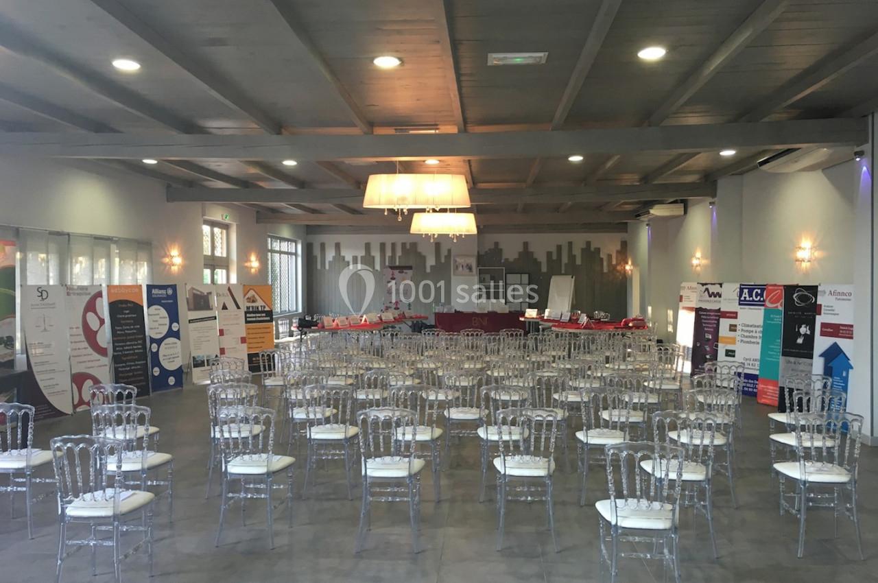 Salle de conférence aménagée avec des chaises transparentes et des stands promotionnels alignés au fond.