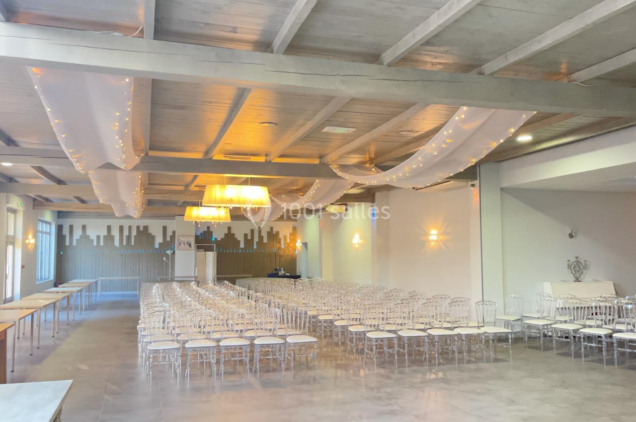 Salle de réception lumineuse avec des rangées de chaises transparentes, des guirlandes lumineuses et un plafond en bois…