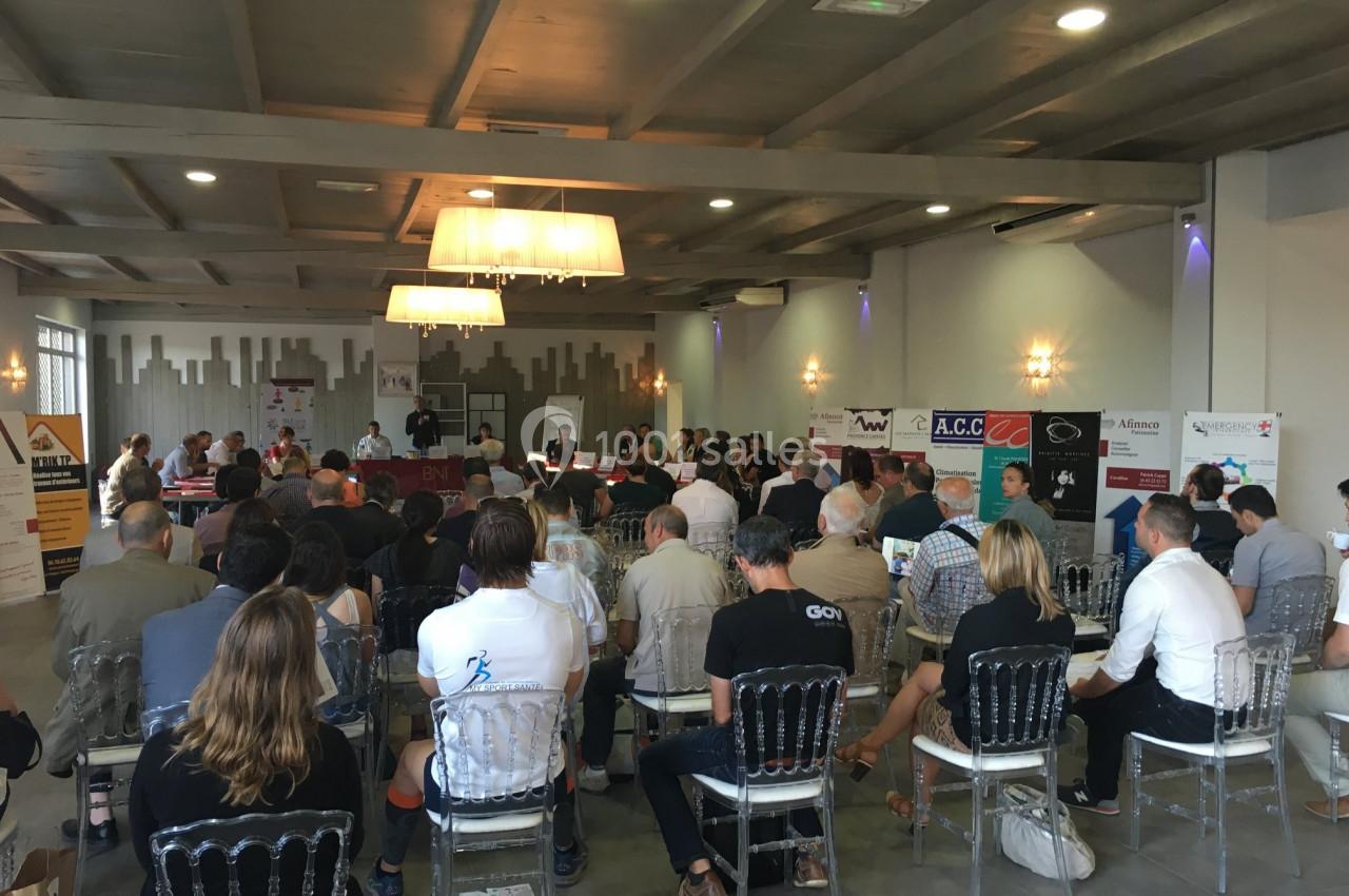 Des personnes assistent à une réunion ou conférence dans une salle lumineuse avec des affiches et des logos en arrière-plan.