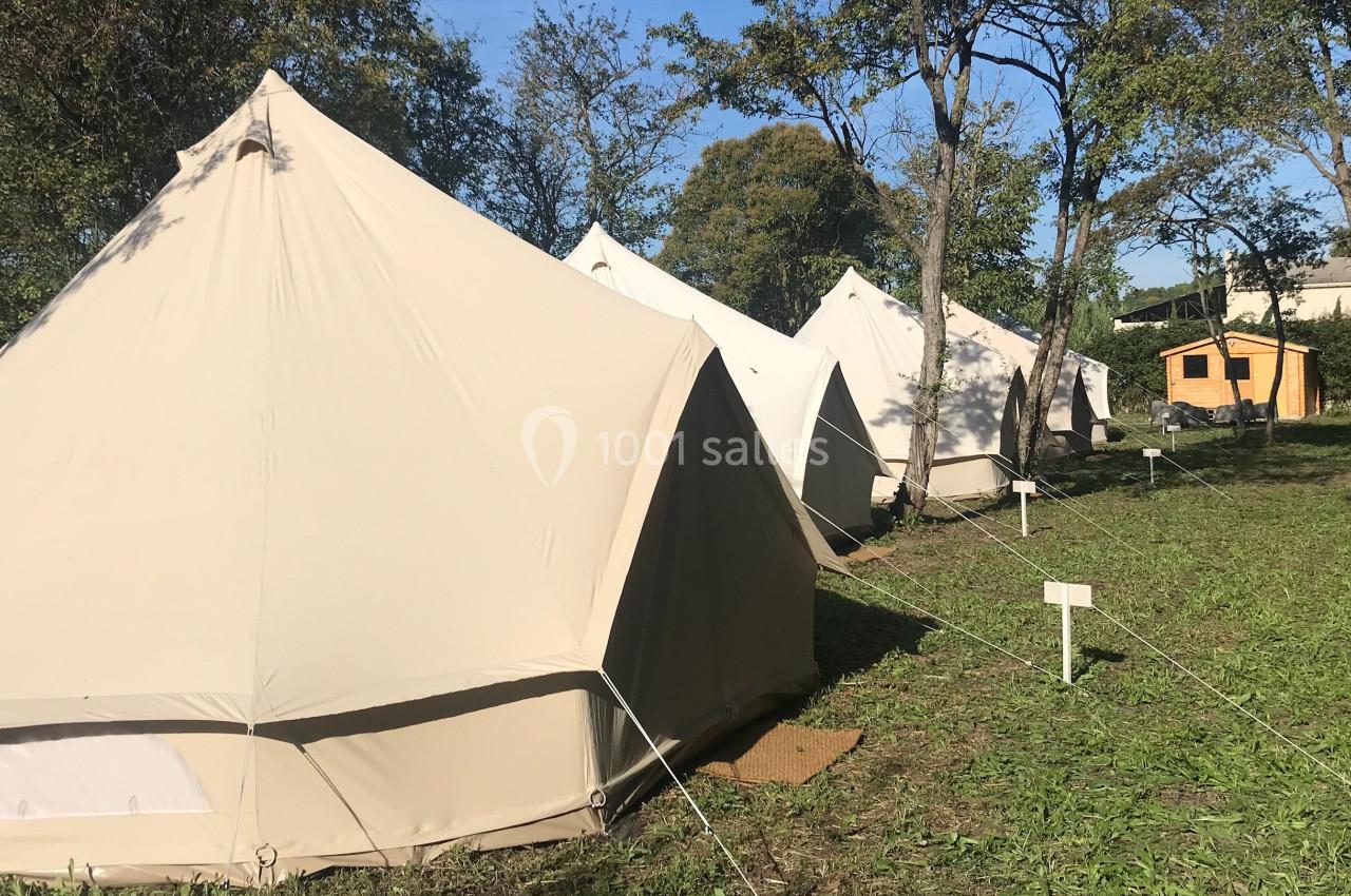 Tentes beige en toile installées en rangée sur une pelouse entourée d'arbres, par une journée ensoleillée.