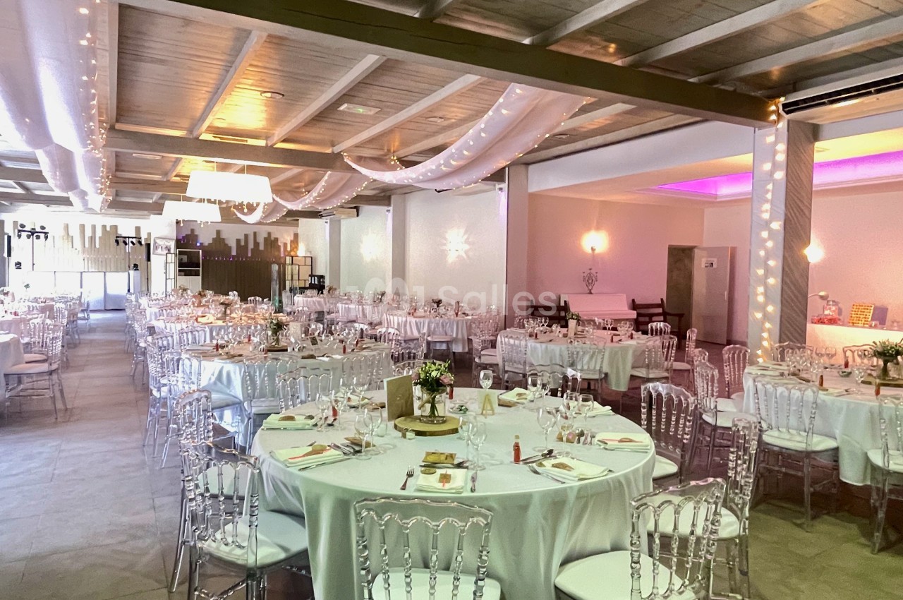 Salle de réception décorée avec des tables rondes dressées, des chaises transparentes et un éclairage chaleureux.