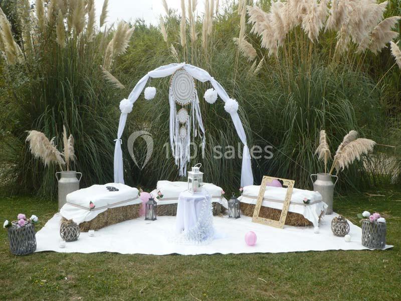 Location salle Saint-Rémy-de-Provence (Bouches-du-Rhône) - Mas de Jonquerolles #10 Décoration bohème en extérieur avec arche ornée de plumes, coussins, lanternes et cadre doré sur une pelouse.