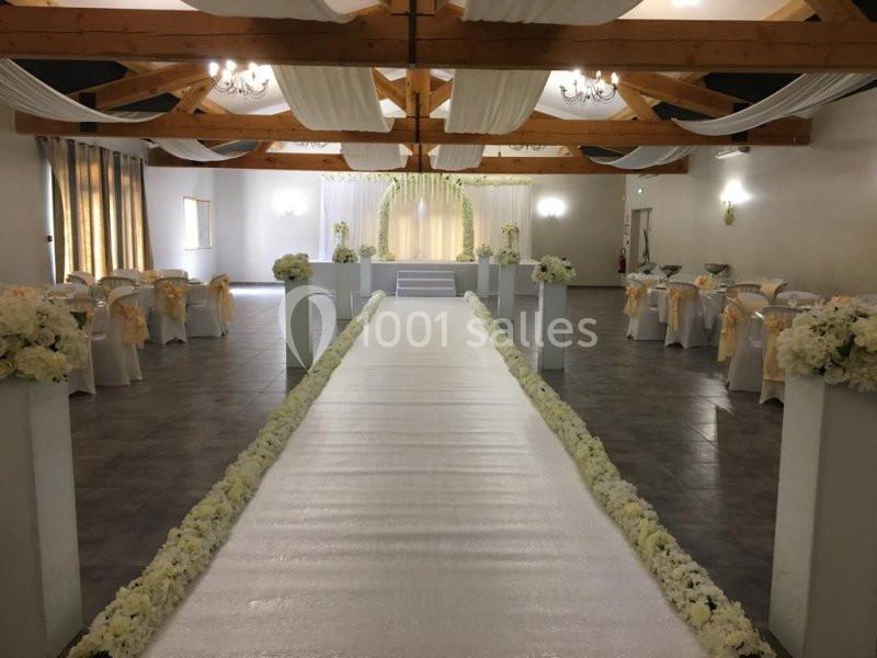 Location salle Saint-Rémy-de-Provence (Bouches-du-Rhône) - Mas de Jonquerolles #20 Salle de réception décorée pour un mariage, avec allée centrale bordée de fleurs blanches et chaises ornées de rubans.