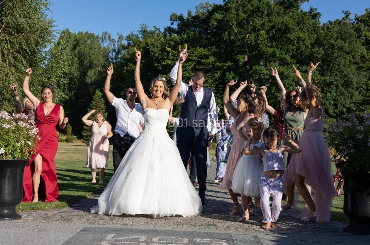 Un groupe de personnes, dont une mariée et un marié, dansant en extérieur sur une allée pavée par une journée ensoleillée.