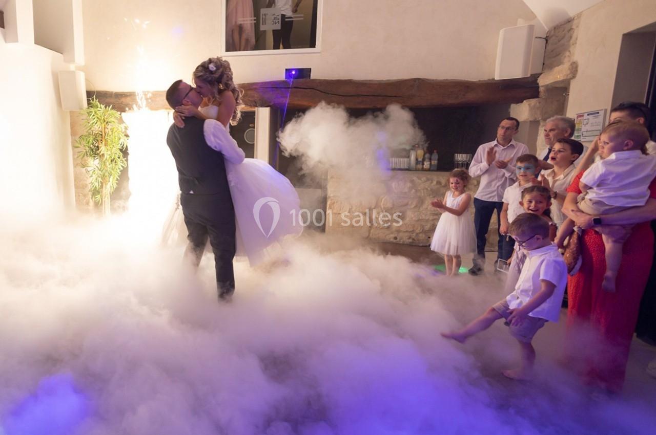 Un couple danse au milieu d'une piste entourée de fumée, observé par des invités dans une salle éclairée.