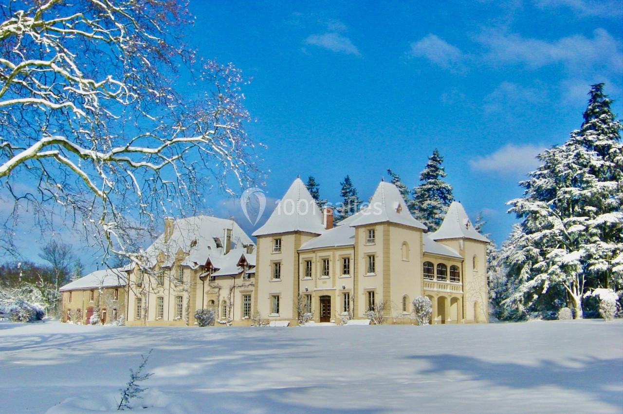 Manoir blanc entouré de neige, avec un ciel bleu clair et des arbres partiellement recouverts de neige.