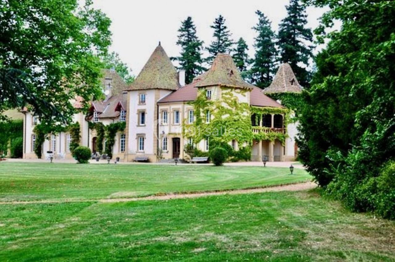 Manoir entouré de pelouses verdoyantes, avec des toits en tuiles et des arbres en arrière-plan.