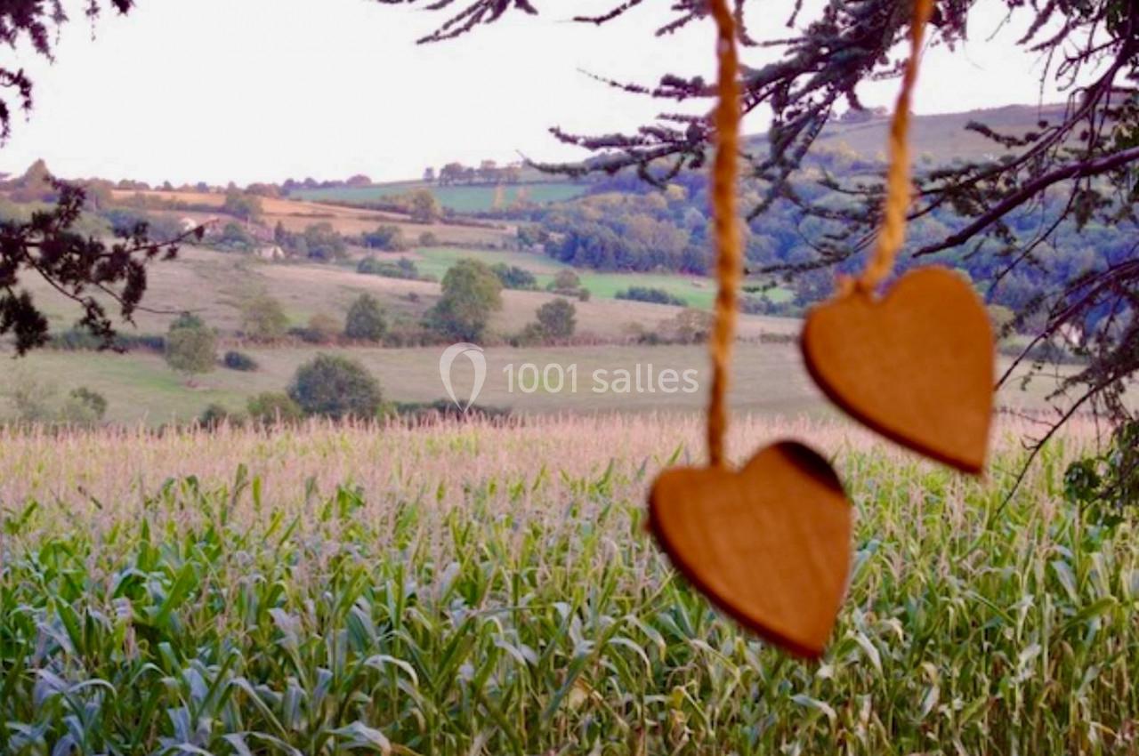 Deux cœurs en bois suspendus devant un champ de maïs et un paysage vallonné en arrière-plan.
