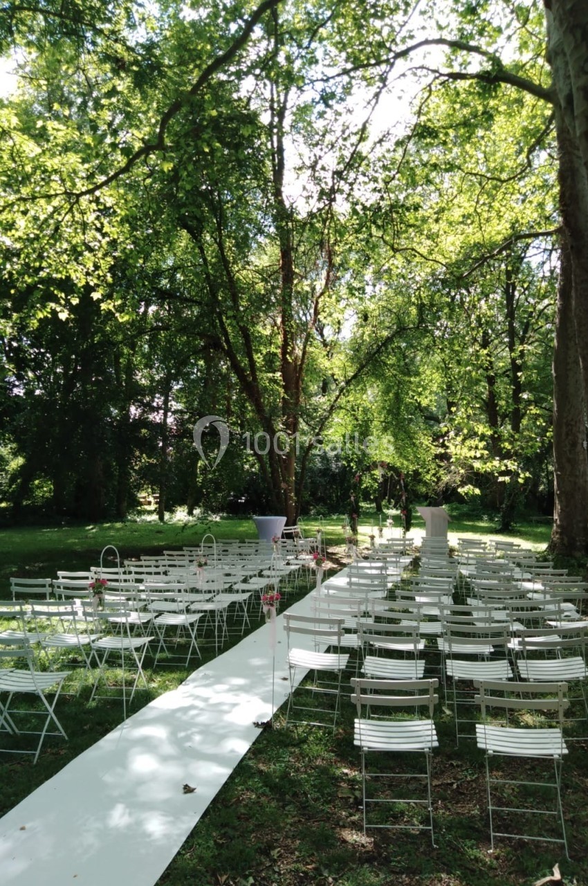 Allée centrale bordée de chaises blanches dans un jardin verdoyant, préparée pour une cérémonie en plein air.