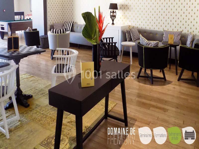 Salle lumineuse avec mobilier moderne, tables, chaises et une console décorée d'un vase contenant des fleurs tropicales.