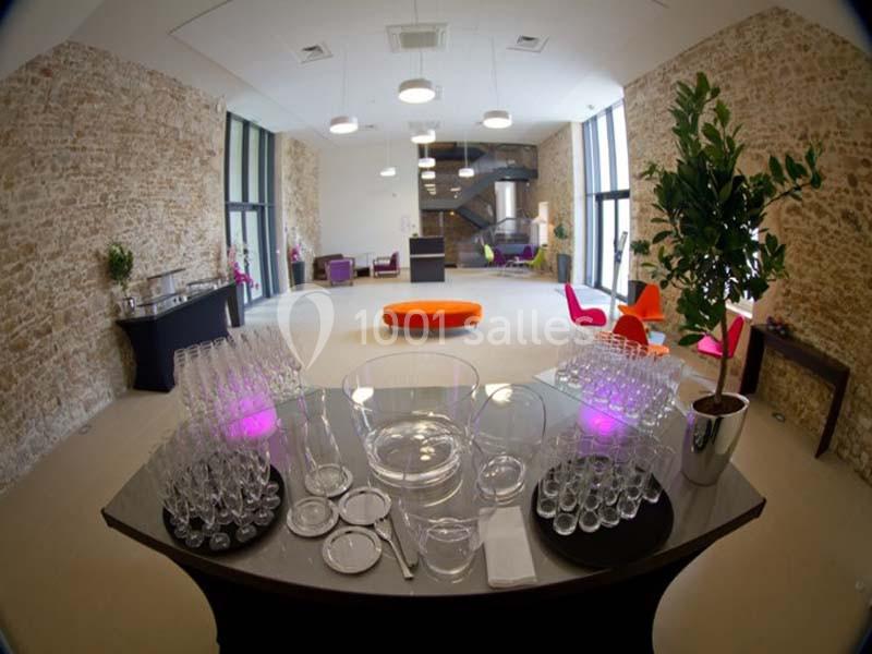 Salle lumineuse avec murs en pierre, mobilier coloré et table dressée avec verres et plats vides au premier plan.