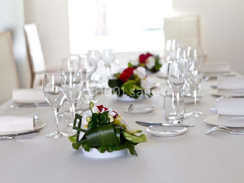 Table dressée avec vaisselle élégante, verres à pied, serviettes blanches et décorations florales au centre.
