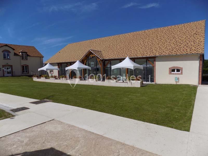 Bâtiment moderne avec toit en tuiles, grandes baies vitrées et terrasses ombragées par des voiles blanches, entouré de…