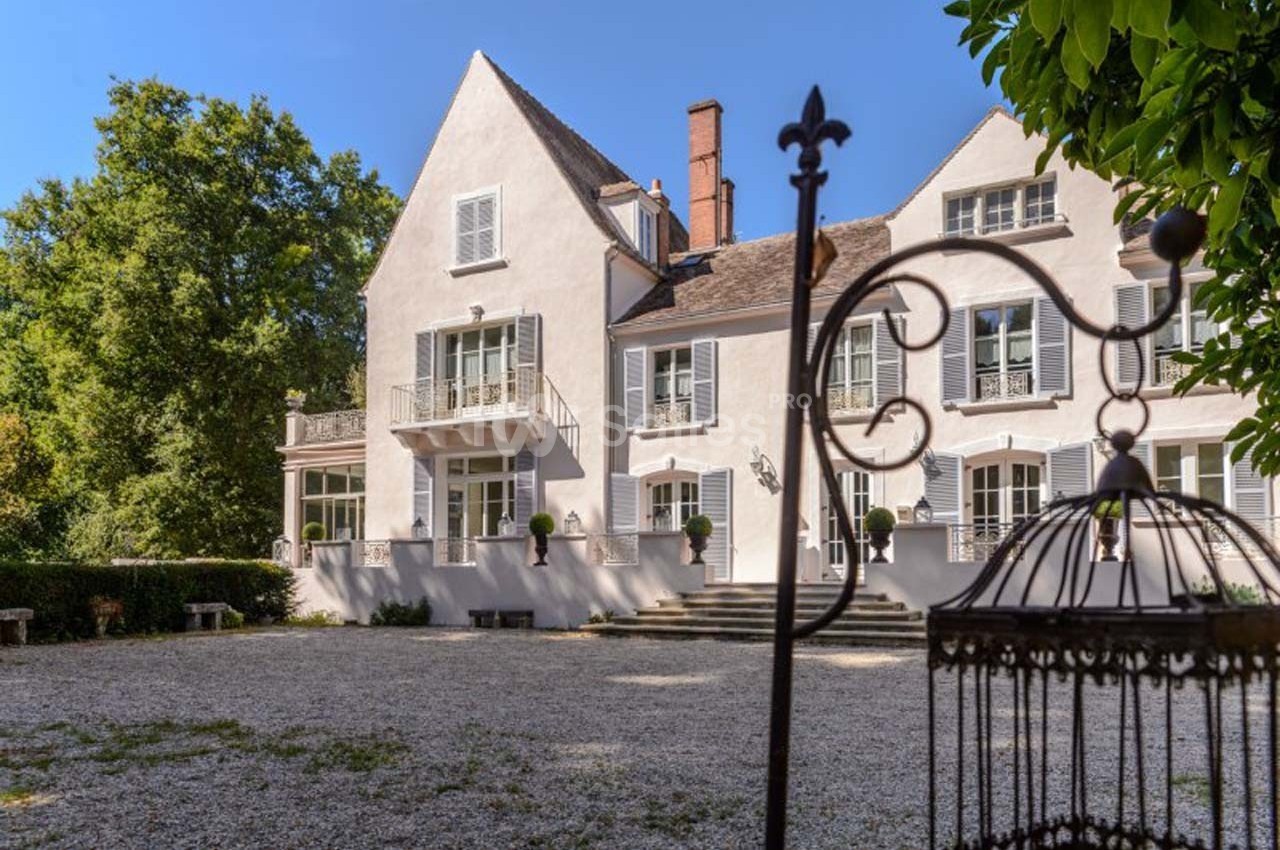Façade d'une maison de style traditionnel avec un jardin gravillonné et des arbres en arrière-plan.