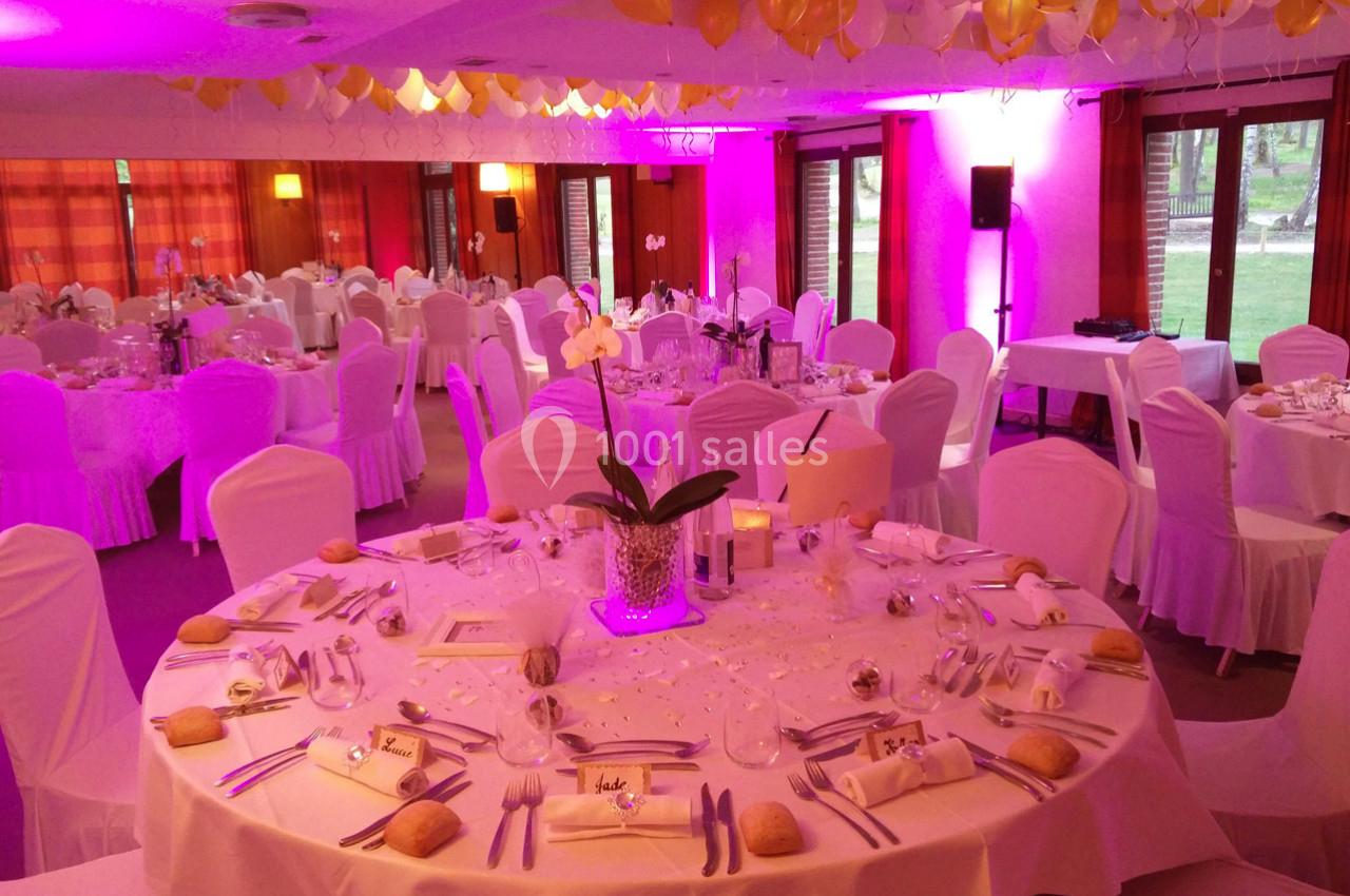 Salle de réception décorée avec des ballons jaunes et blancs, tables rondes dressées avec nappes blanches et orchidées.