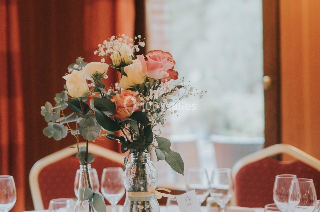 Bouquet de fleurs colorées au centre d'une table dressée avec des verres dans une salle éclairée par la lumière naturelle.