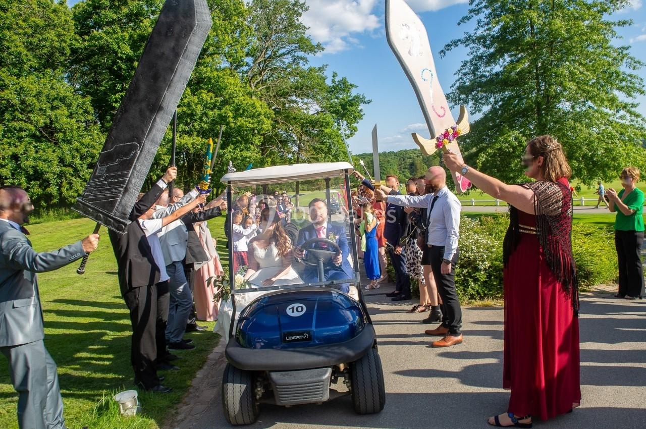 Un homme dans une voiturette de golf passe sous une haie d'honneur formée par des invités brandissant des épées géantes.