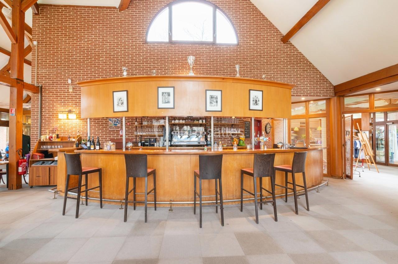 Bar en bois avec tabourets alignés, situé dans une grande pièce lumineuse avec murs en briques et plafond voûté.