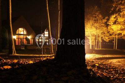 Miniature Location salle Janvry (Essonne) - Golf de Marivaux #35 Maison en bois éclairée la nuit, entourée d'arbres illuminés, sous un ciel nuageux avec la lune visible.