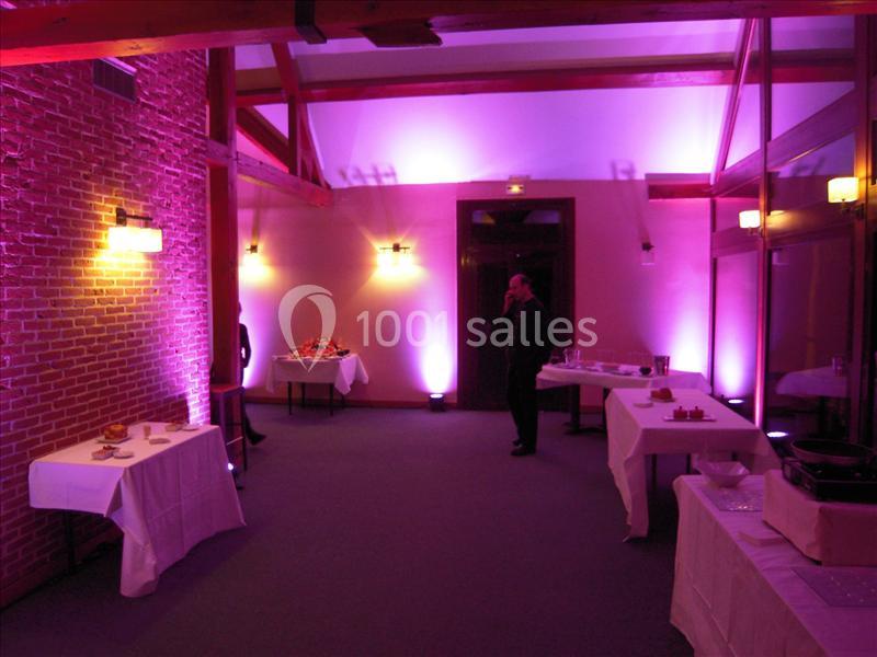 Salle de réception avec murs en briques, éclairage violet et tables dressées pour un buffet.