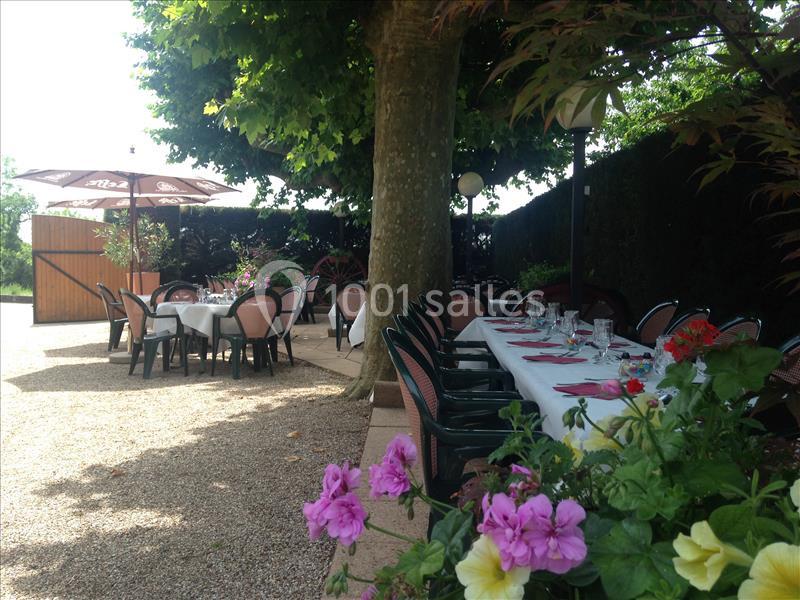 Terrasse ombragée avec tables dressées pour un repas, entourée de fleurs et de parasols.
