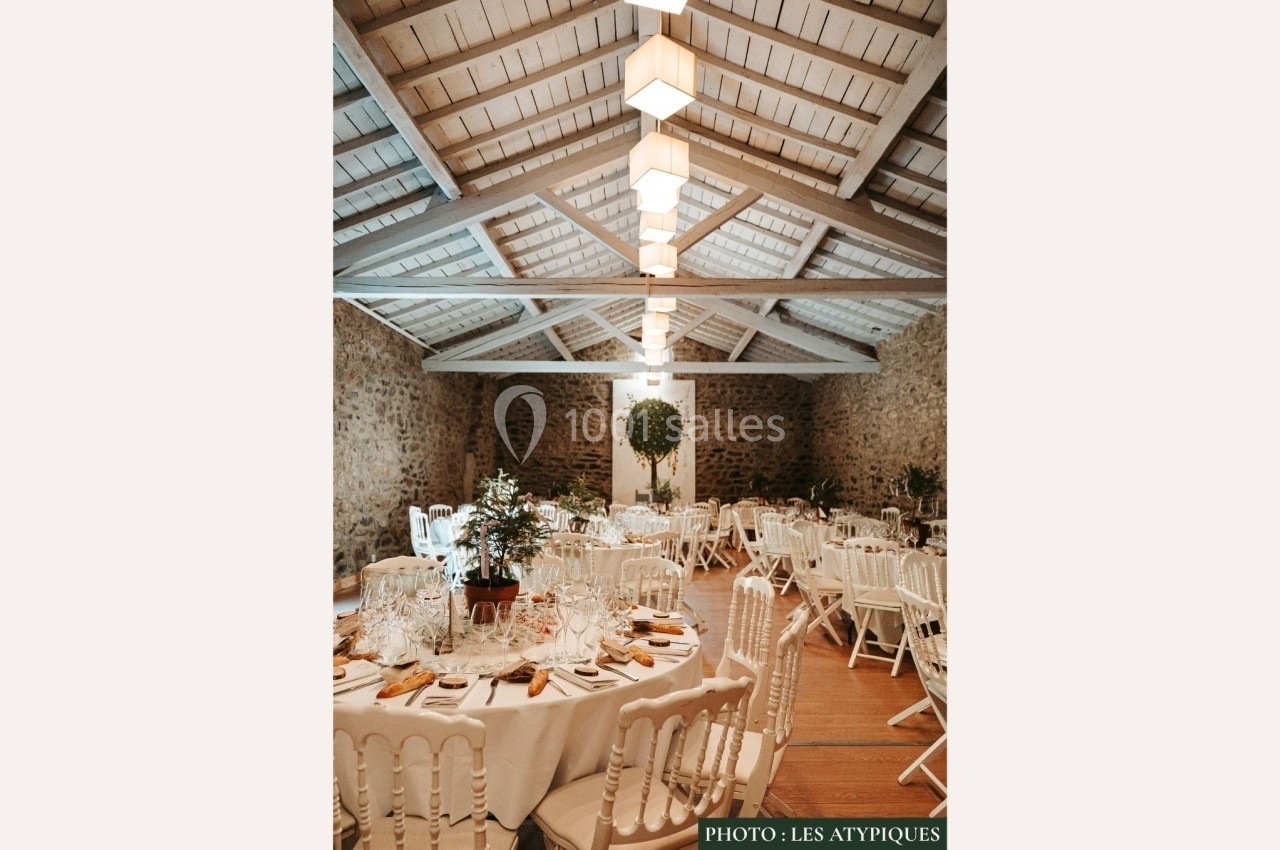 Salle de réception avec tables rondes dressées, chaises blanches et plafond en bois sous une lumière chaleureuse.