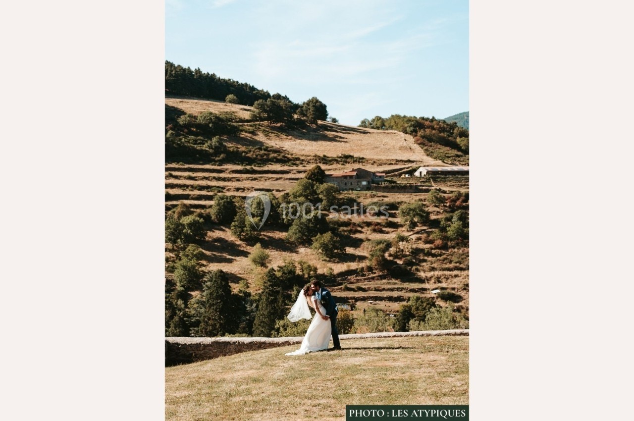 Un couple en tenue de mariage se tient dans un paysage rural avec des collines et des terrasses en arrière-plan.
