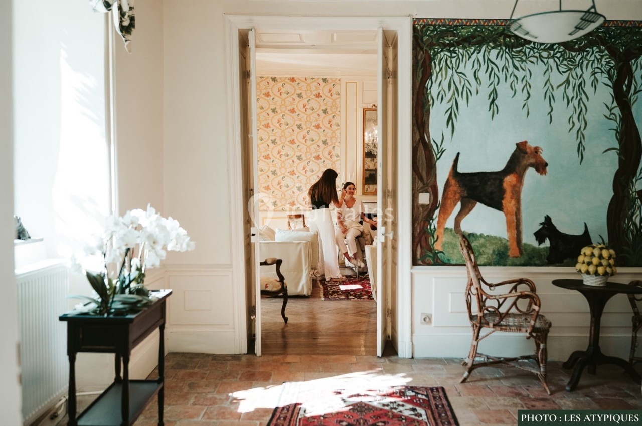 Une pièce lumineuse avec vue sur un salon décoré, des personnes discutant au fond près d'une fresque murale.