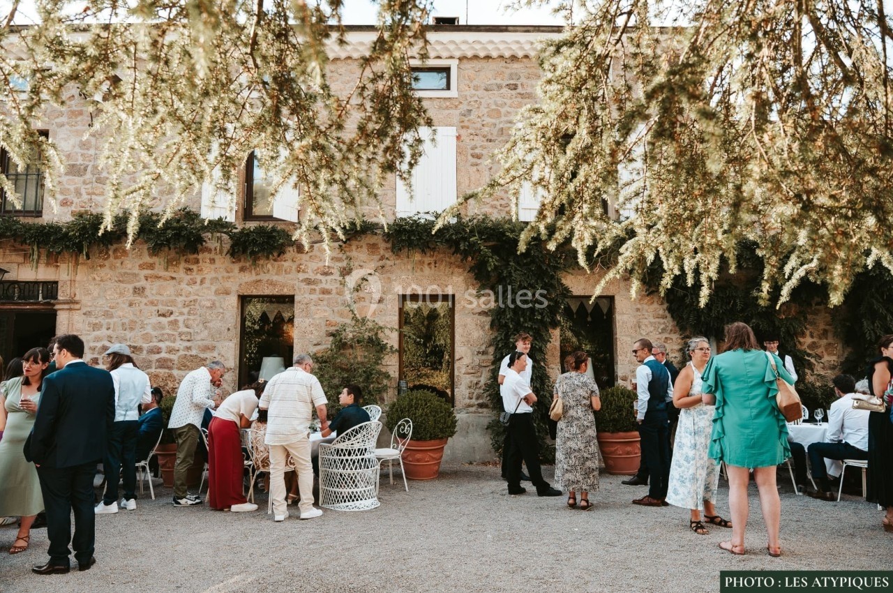 Groupe de personnes discutant et partageant un moment convivial dans la cour d'un bâtiment en pierre décoré de verdure.
