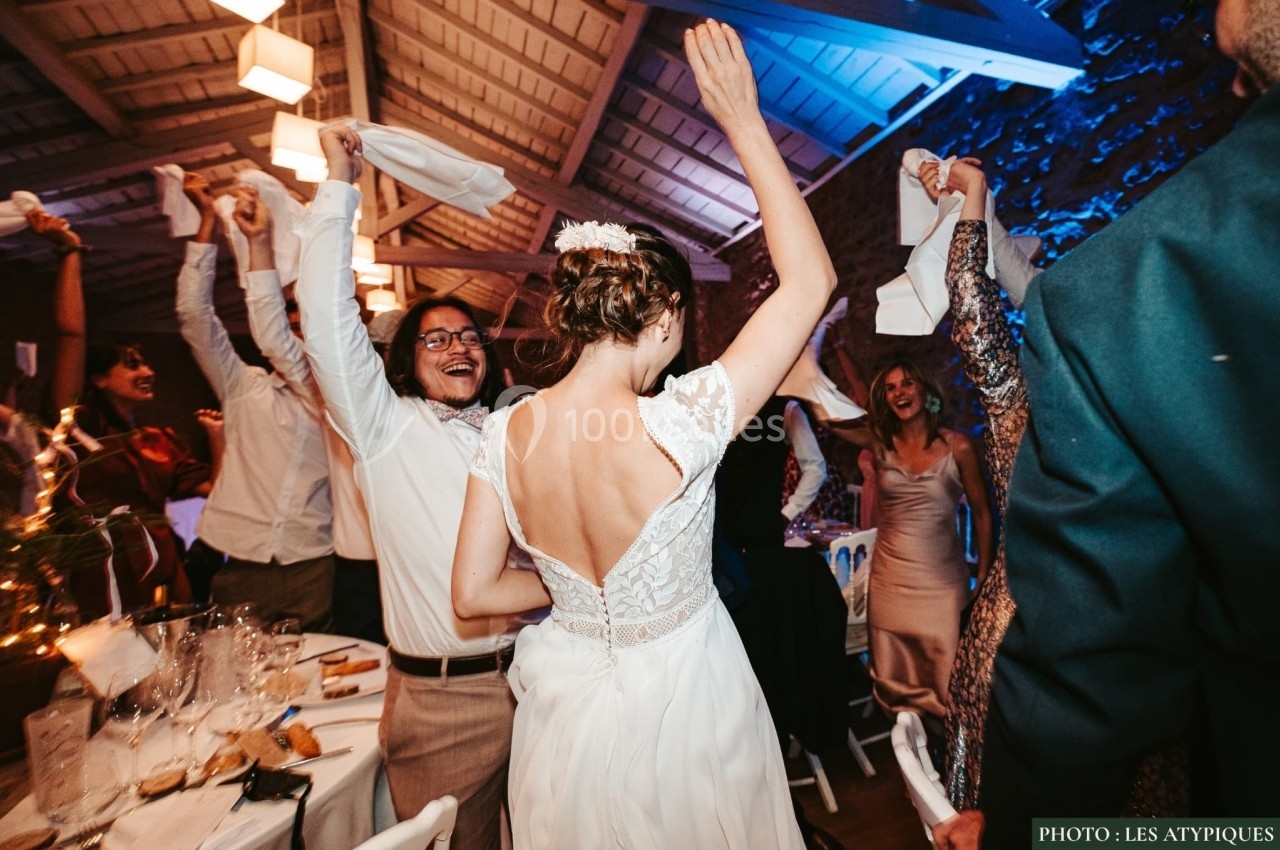 Des invités dansent et célèbrent lors d'un mariage dans une salle éclairée, avec une mariée au centre.