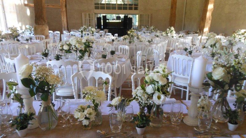 Salle de réception décorée avec des tables rondes, nappes blanches et bouquets de fleurs blanches et vertes.