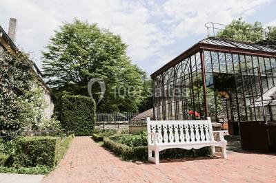 Miniature Location salle Verderonne (Oise) - Domaine de Verderonne #29 Serre illuminée au crépuscule, entourée de murs en pierre et d'arbres, avec une tour en arrière-plan.
