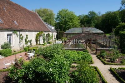 Miniature Location salle Verderonne (Oise) - Domaine de Verderonne #14 Serre illuminée au crépuscule, entourée de murs en pierre et d'arbres, avec une tour en arrière-plan.