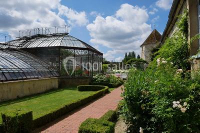 Miniature Location salle Verderonne (Oise) - Domaine de Verderonne #30 Serre illuminée au crépuscule, entourée de murs en pierre et d'arbres, avec une tour en arrière-plan.