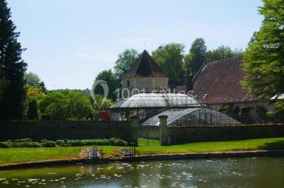Miniature Location salle Verderonne (Oise) - Domaine de Verderonne #18 Serre illuminée au crépuscule, entourée de murs en pierre et d'arbres, avec une tour en arrière-plan.
