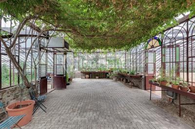 Miniature Location salle Verderonne (Oise) - Domaine de Verderonne #16 Serre illuminée au crépuscule, entourée de murs en pierre et d'arbres, avec une tour en arrière-plan.