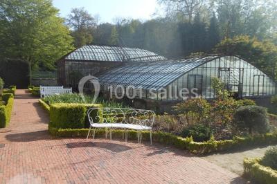 Miniature Location salle Verderonne (Oise) - Domaine de Verderonne #27 Serre illuminée au crépuscule, entourée de murs en pierre et d'arbres, avec une tour en arrière-plan.
