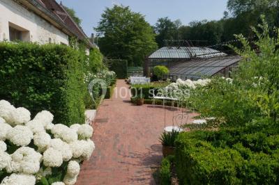 Miniature Location salle Verderonne (Oise) - Domaine de Verderonne #8 Serre illuminée au crépuscule, entourée de murs en pierre et d'arbres, avec une tour en arrière-plan.