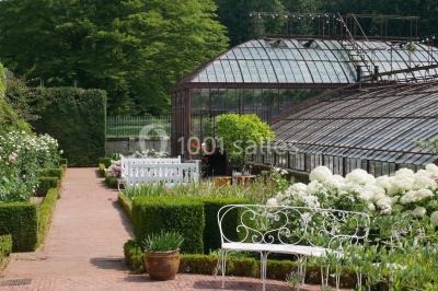 Miniature Location salle Verderonne (Oise) - Domaine de Verderonne #24 Serre illuminée au crépuscule, entourée de murs en pierre et d'arbres, avec une tour en arrière-plan.