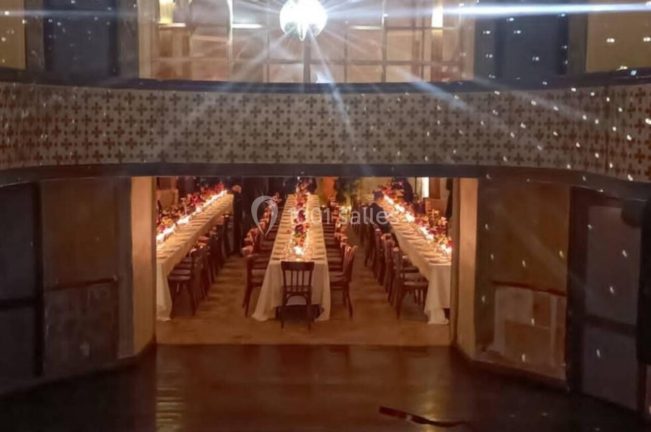 Vue depuis une cabine DJ sur une salle de réception éclairée par une boule à facettes, avec tables dressées en arrière-plan.