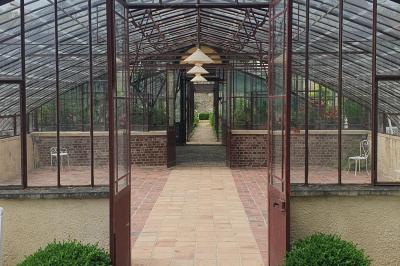 Miniature Location salle Verderonne (Oise) - Domaine de Verderonne #35 Serre illuminée au crépuscule, entourée de murs en pierre et d'arbres, avec une tour en arrière-plan.