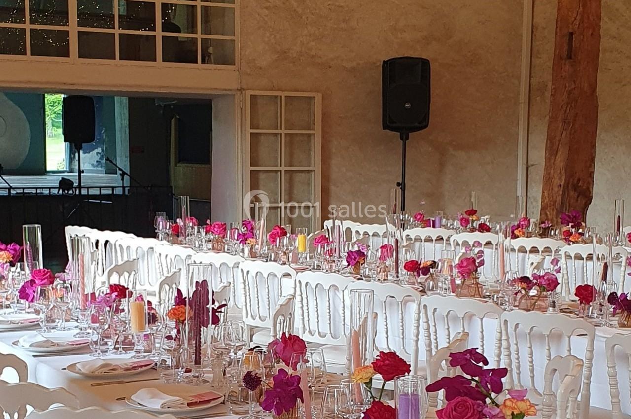 Salle de réception décorée avec des tables blanches alignées, ornées de fleurs colorées et de vaisselle élégante.