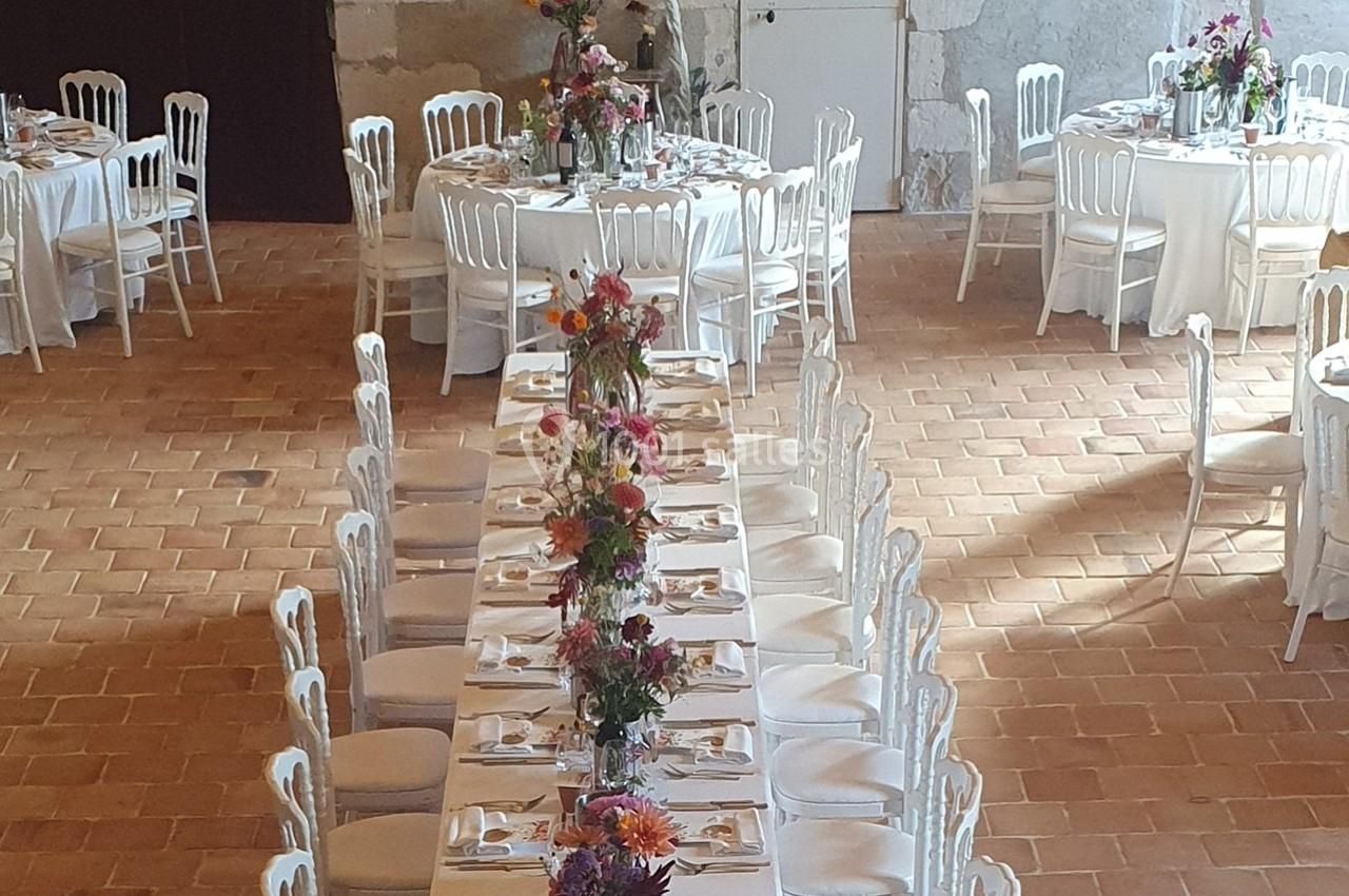 Tables de réception décorées de fleurs colorées, disposées dans une salle au sol en pierre et aux murs clairs.